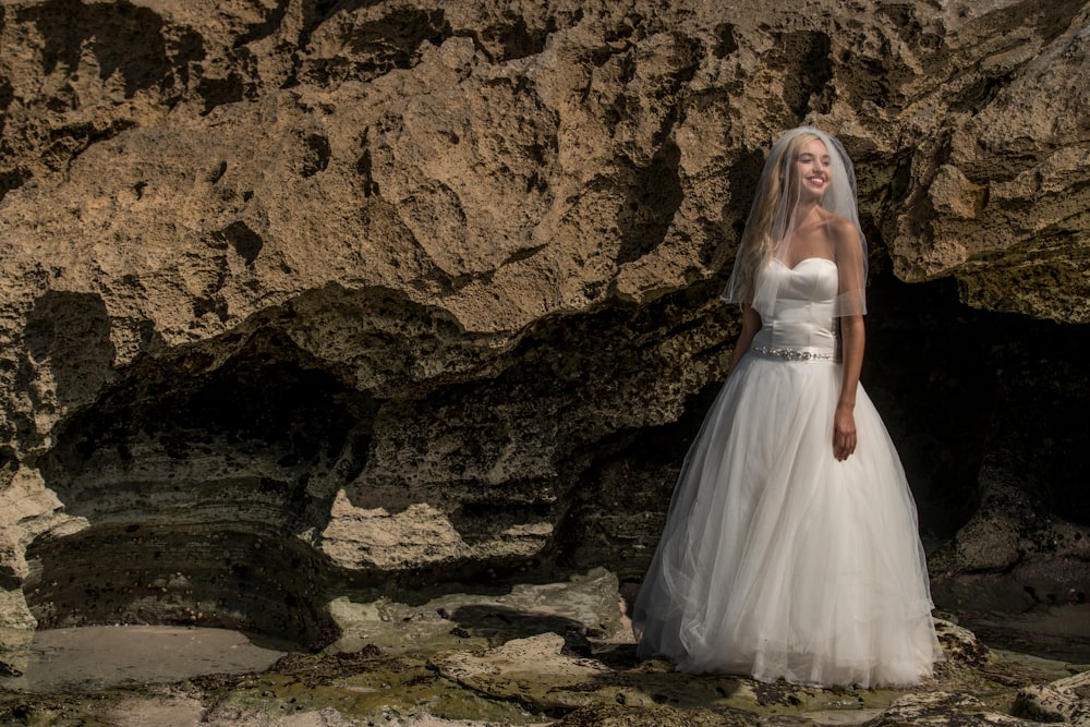 woman in white wedding dress standing on brown rock