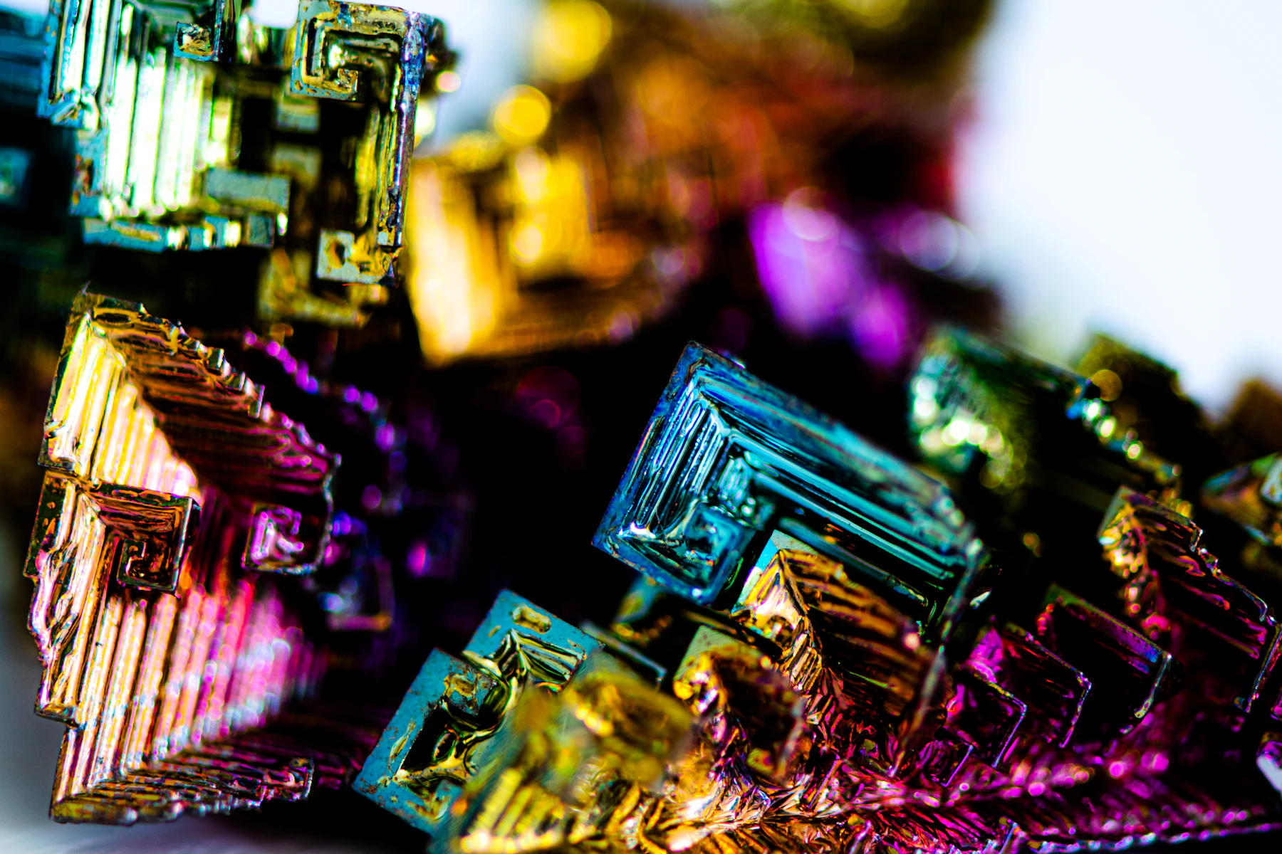 Close-up of bismuth crystals, their square spiral steps shining gold, magenta and teal