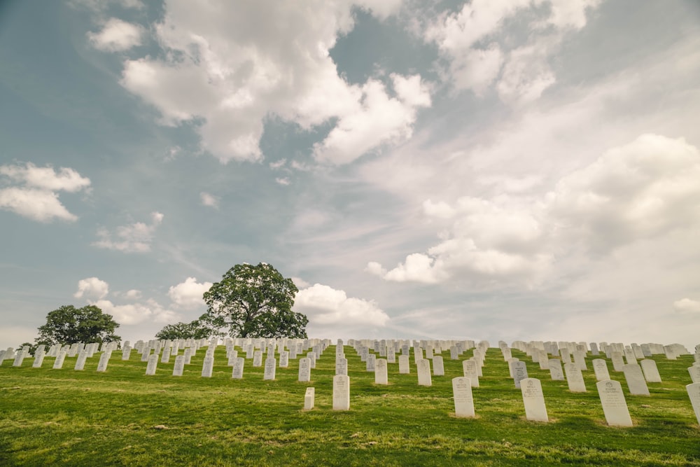 green grass field with white cross under white clouds during daytime