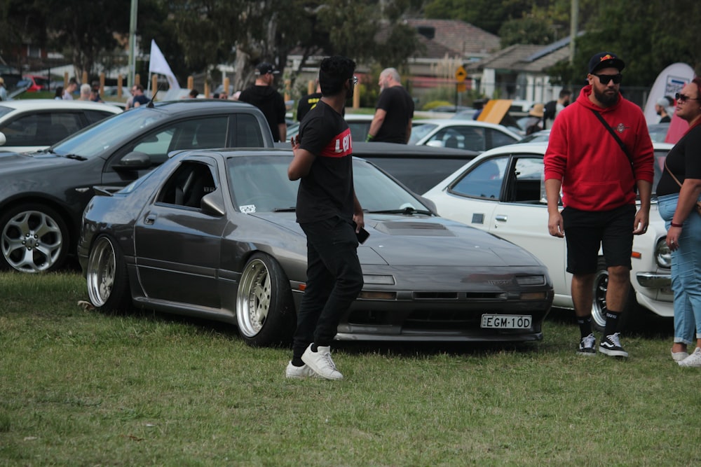 man in black t-shirt and black pants standing beside gray car during daytime