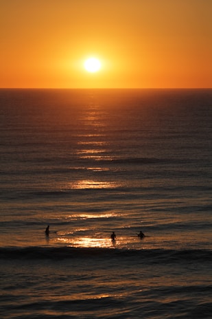 A vibrant sunset over the ocean with surfers in silhouette.