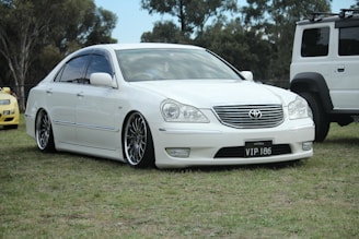 A sleek Toyota sedan parked outside the Crystal Wheels showroom in Delhi on a sunny day.