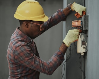 man in brown and white plaid dress shirt and yellow hard hat holding black and orange