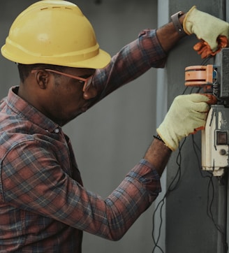 man in brown and white plaid dress shirt and yellow hard hat holding black and orange