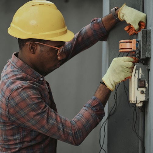 man in brown and white plaid dress shirt and yellow hard hat holding black and orange