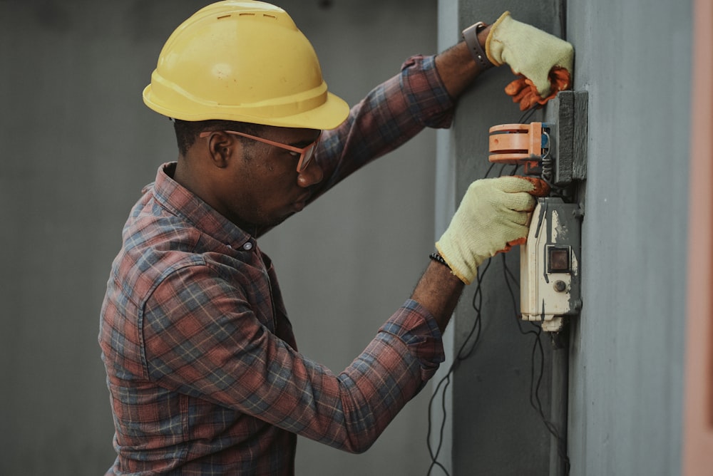 man in brown and white plaid dress shirt and yellow hard hat holding black and orange