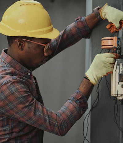 man in brown and white plaid dress shirt and yellow hard hat holding black and orange