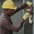 man in brown and white plaid dress shirt and yellow hard hat holding black and orange