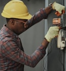 man in brown and white plaid dress shirt and yellow hard hat holding black and orange