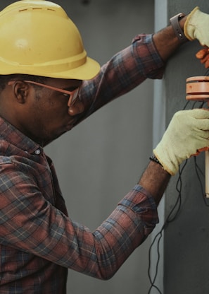 man in brown and white plaid dress shirt and yellow hard hat holding black and orange