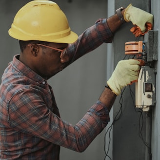 man in brown and white plaid dress shirt and yellow hard hat holding black and orange