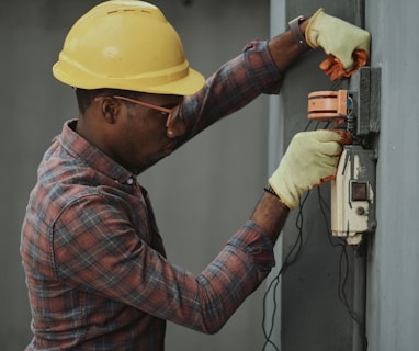 man in brown and white plaid dress shirt and yellow hard hat holding black and orange