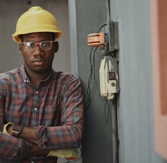 worker in blue white and red plaid button up shirt wearing yellow hard hat holding black