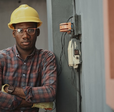 worker in blue white and red plaid button up shirt wearing yellow hard hat holding black