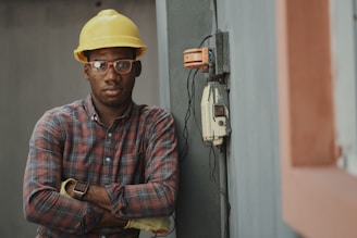 worker in blue white and red plaid button up shirt wearing yellow hard hat holding black