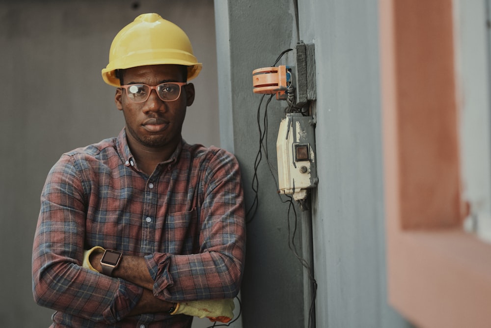 Homme en chemise bleue blanche et rouge boutonnée portant un casque jaune tenant du noir