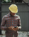 man in red blue and white plaid dress shirt wearing yellow hat holding black smartphone
