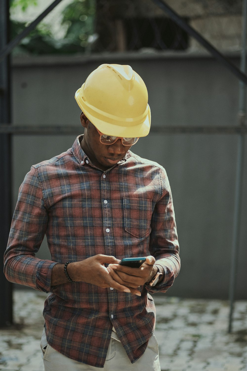 Hombre con camisa de vestir a cuadros roja, azul y blanca con sombrero amarillo sosteniendo un teléfono inteligente negro