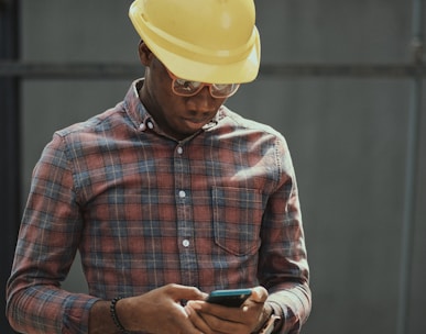 man in red blue and white plaid dress shirt wearing yellow hat holding black smartphone