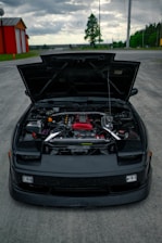 Scotty and Justin working together on a sleek black sedan in a sunny driveway.