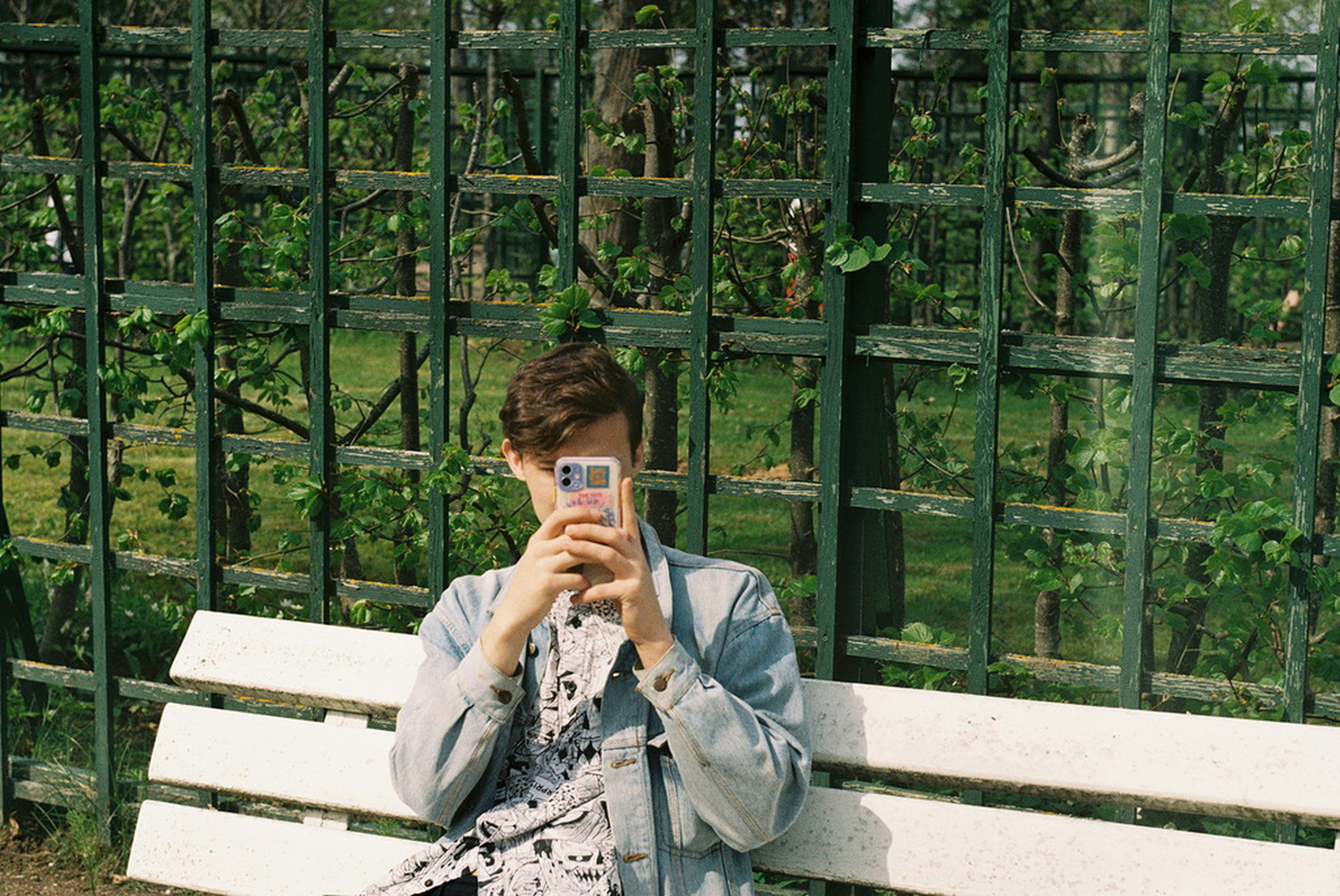 teenager sitting on park bench looking away from smartphone