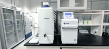 A laboratory setting featuring advanced water purification equipment and storage cabinets. The lab is clean and organized with several machines on a black countertop. There are large storage units in the background.