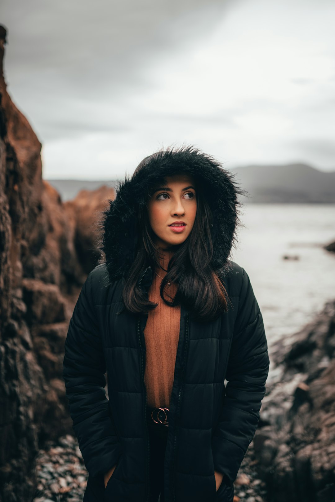 woman in black leather jacket standing near brown rock formation during daytime