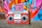 A vintage red boombox with cassette player and twin speakers is set against a vibrant graffiti-covered wall. The wall displays a mix of colors including pink, blue, and orange, enhancing the retro aesthetic.