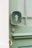 A close-up of a green door with a brass door handle, a keyhole, and an attached dark green plaque embossed with a golden symbol or letter.