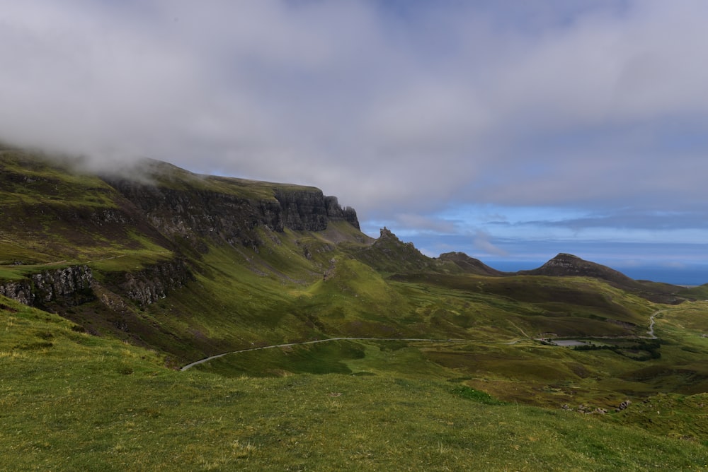 green grass field near mountain under cloudy sky during daytime