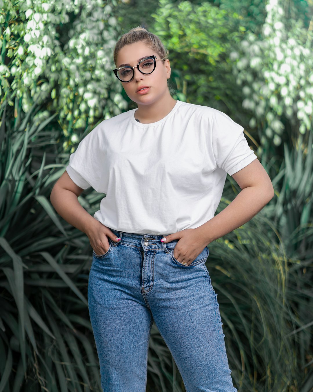 woman in white crew neck t-shirt and blue denim jeans standing near green plants during