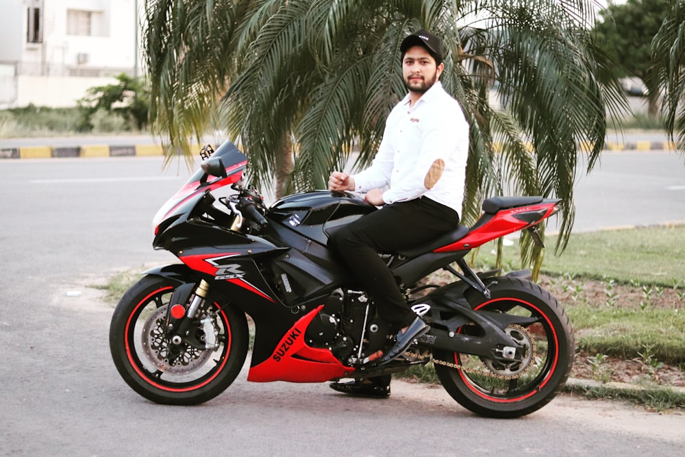 man in white dress shirt riding red and black sports bike