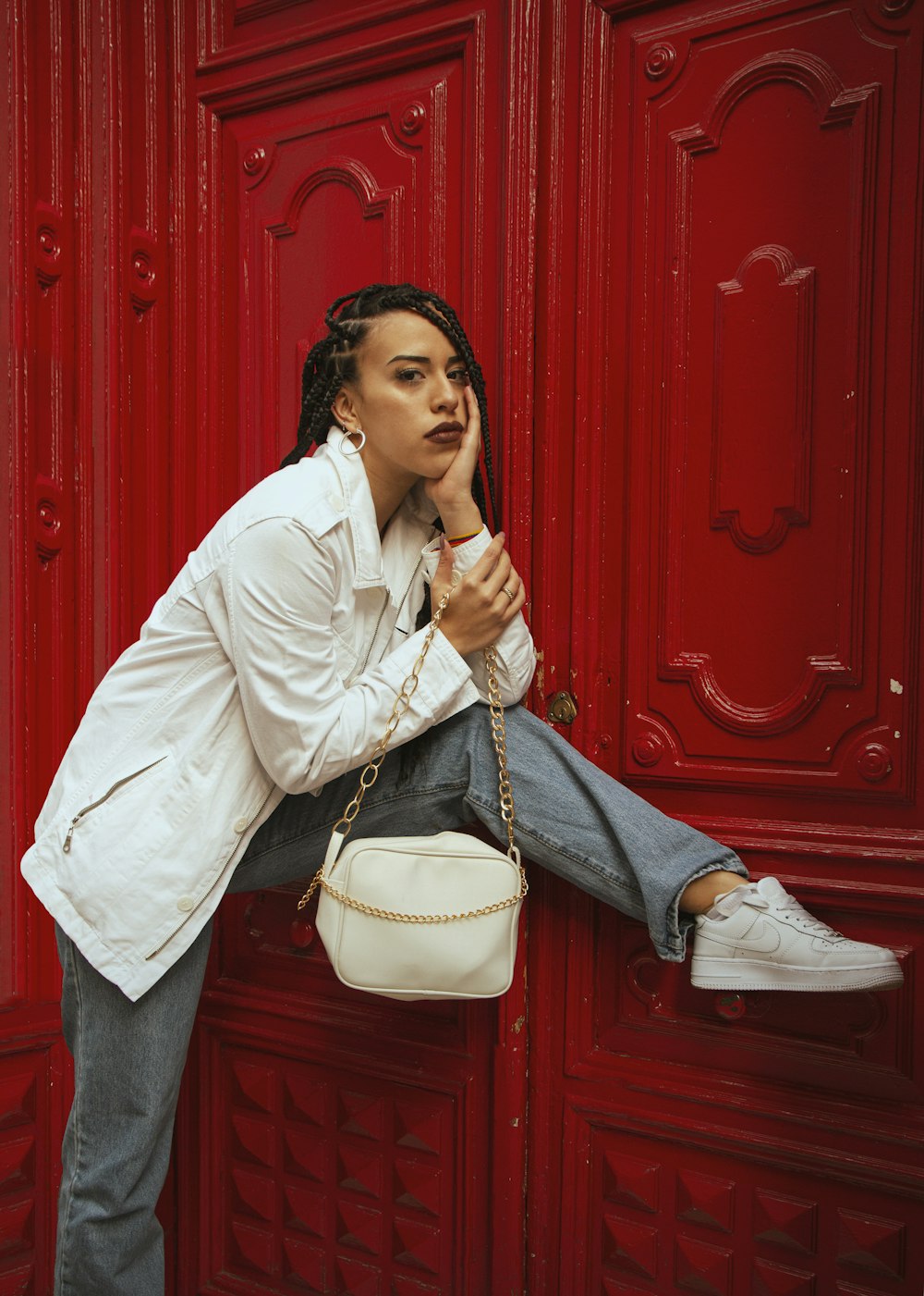 woman in white dress shirt and blue denim jeans sitting on red wooden door