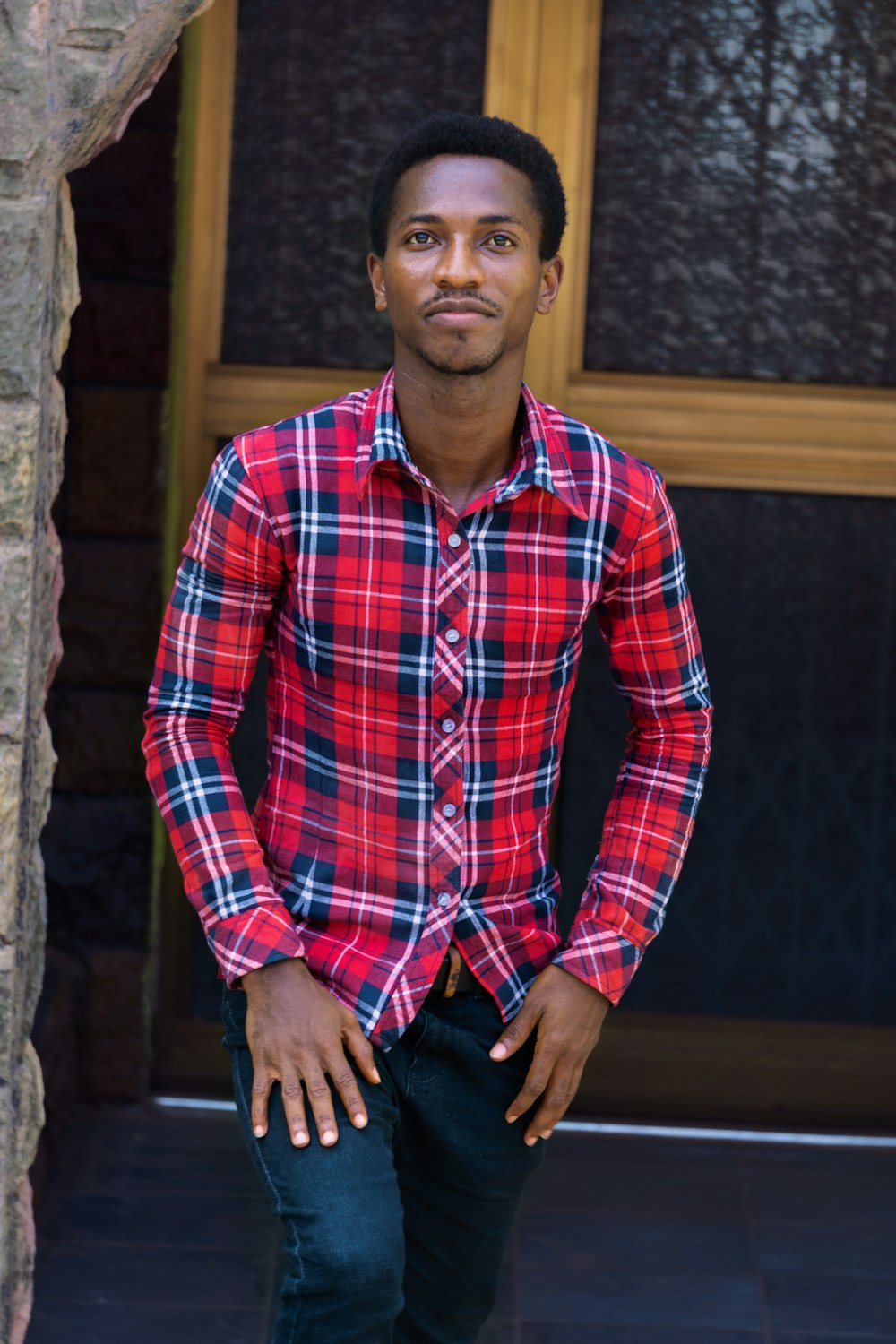 man in blue red and white plaid dress shirt and black denim jeans sitting on brown