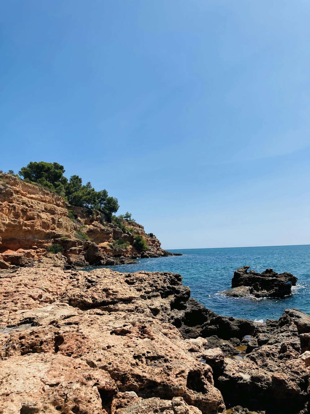 brown rocky mountain beside blue sea under blue sky during daytime