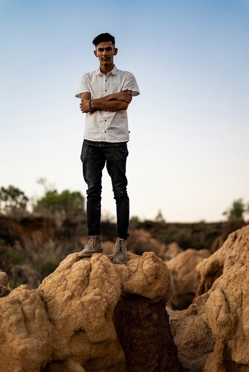 man in white dress shirt and black pants standing on brown rock during daytime