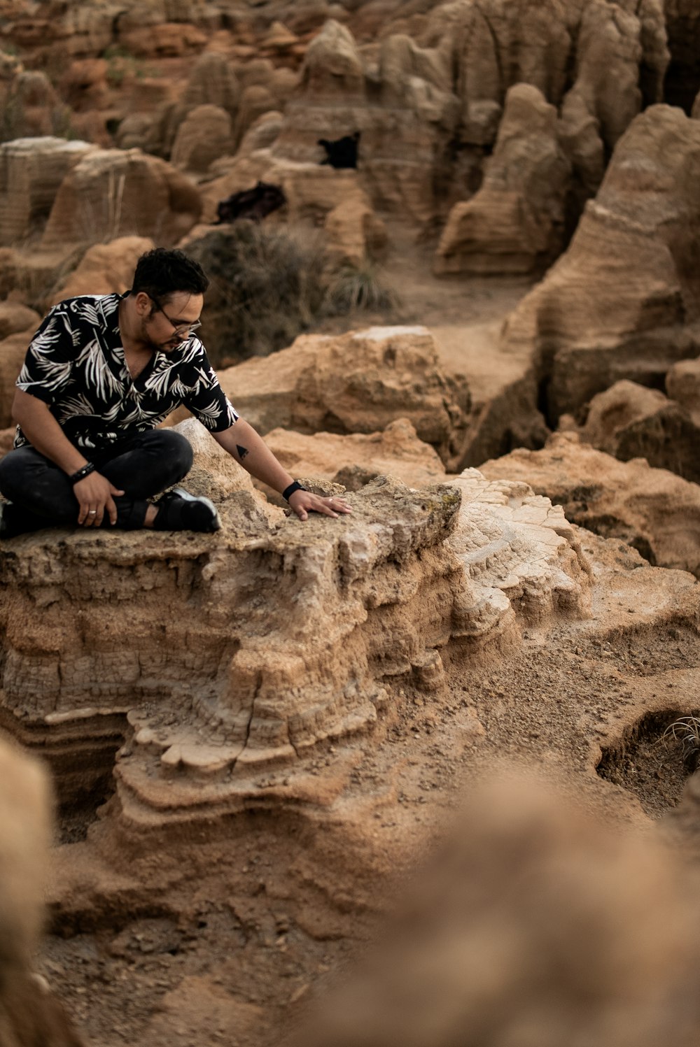 man in black and white plaid button up shirt sitting on brown rock during daytime