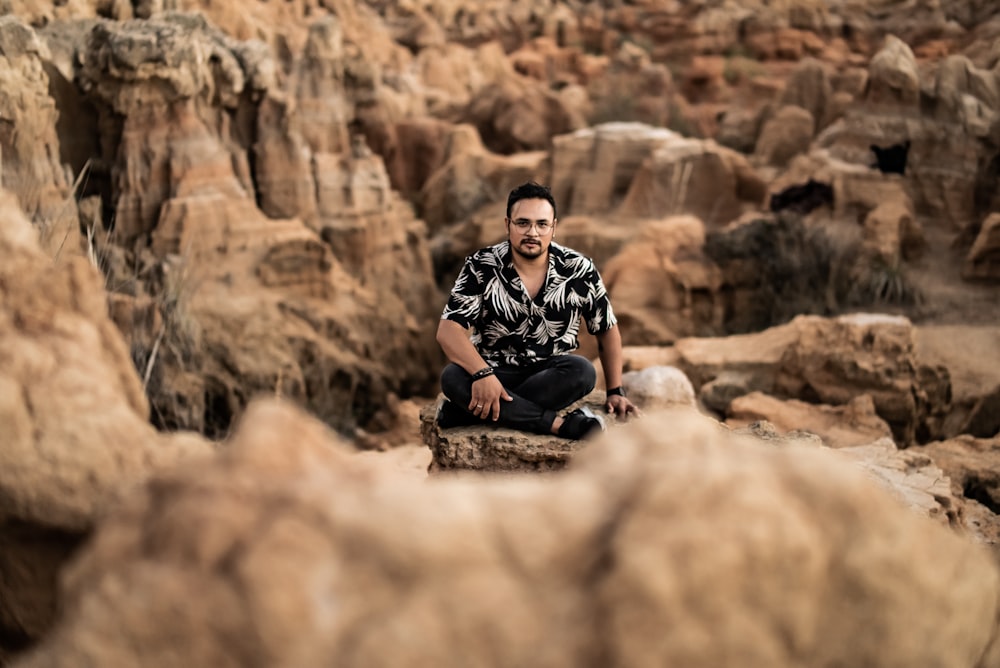 man in black and white checkered button up shirt sitting on brown rock during daytime