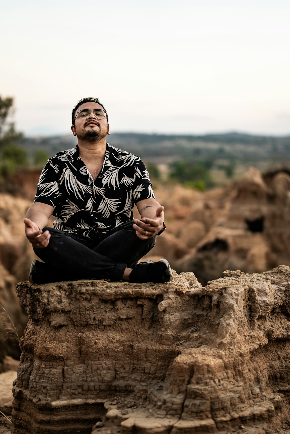 man in black and white floral dress shirt sitting on brown rock during daytime