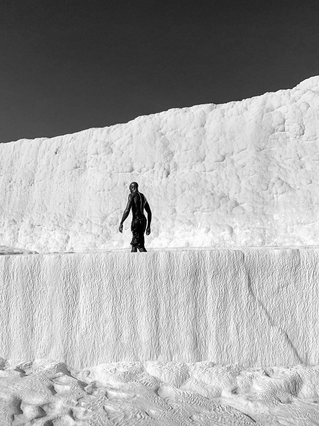 grayscale photo of man in black jacket and pants standing on rock formation