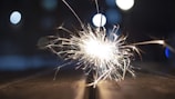 A vibrant sparkler emitting bright sparks against a blurred background with bokeh lights.
