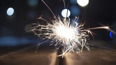 A vibrant sparkler emitting bright sparks against a blurred background with bokeh lights.