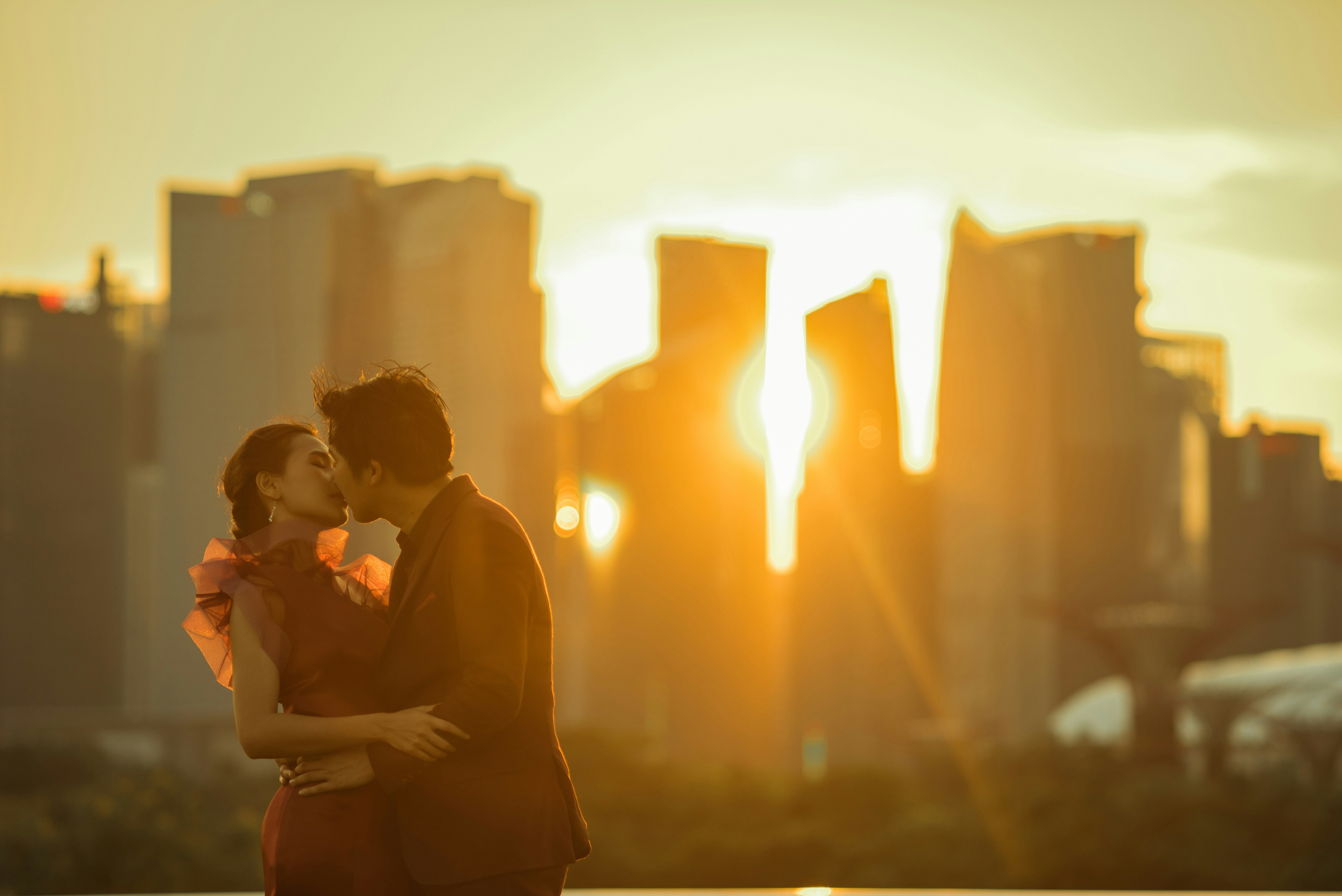 man in black shirt standing and kissing woman in black dress during sunset