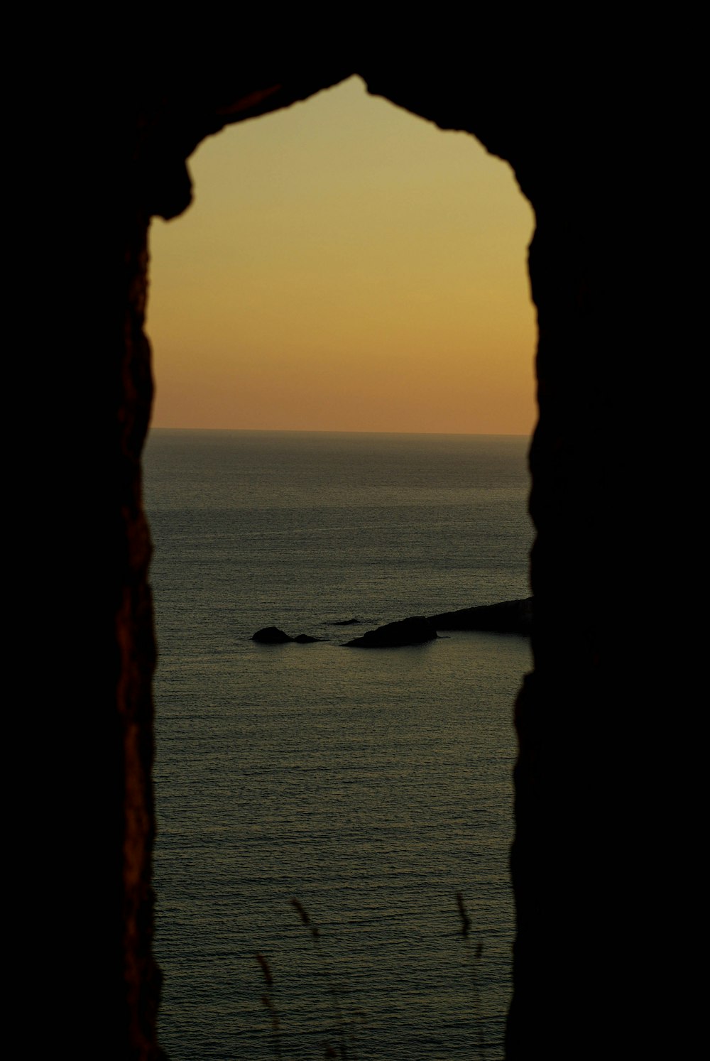 silhouette of rock formation on sea during sunset