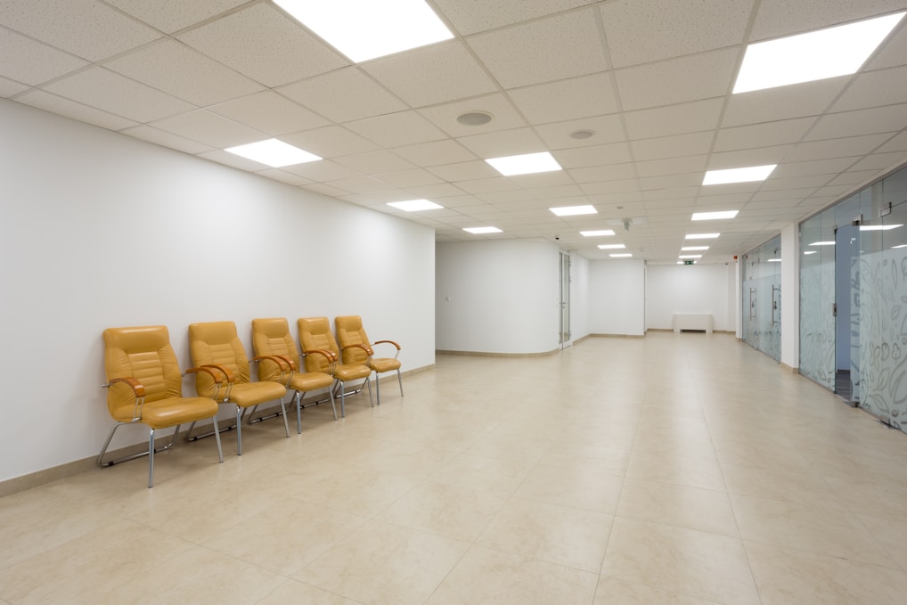 brown and white chairs on a brown tiled floor with large overhead lights and offices on the left