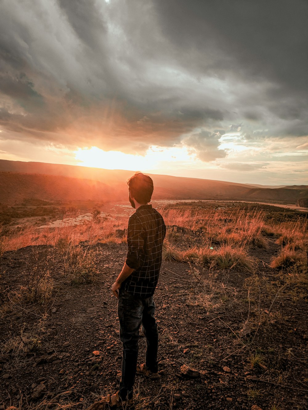 man in brown and black plaid dress shirt standing on green grass field during sunset