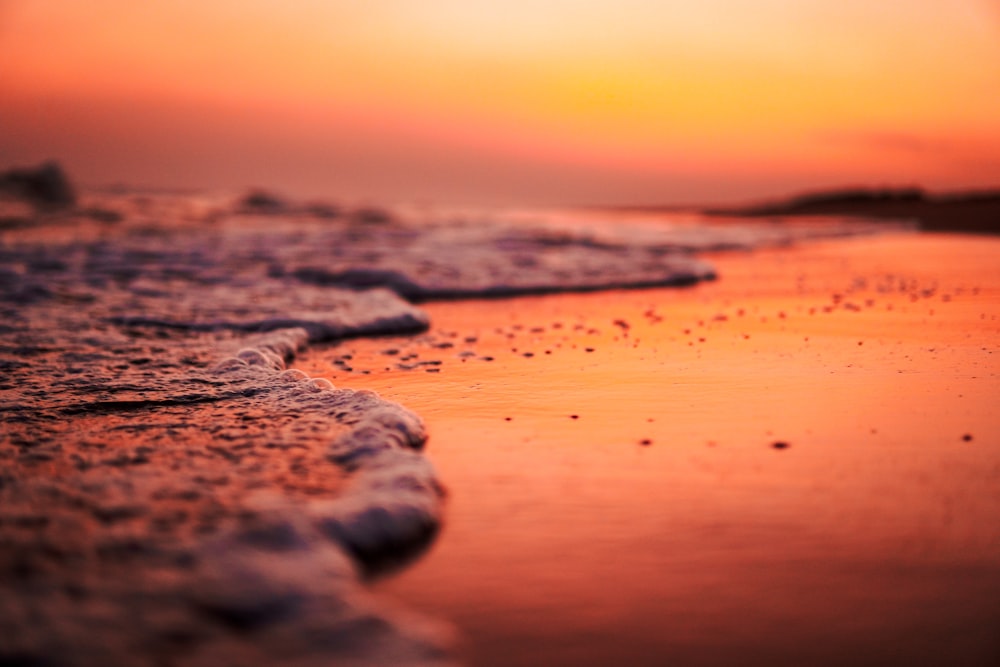 Olas de agua sobre arena marrón durante la puesta de sol