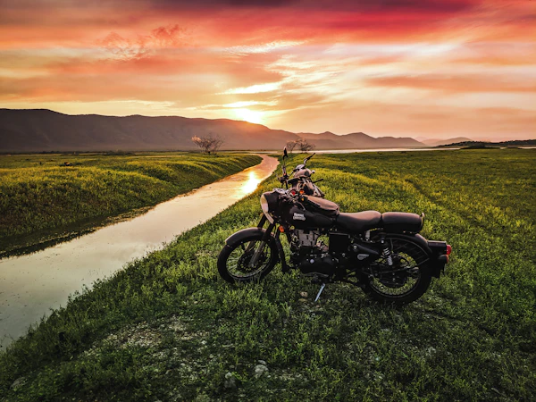 Motorcycle parked by a countryside stream at sunset