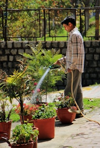 man in blue and white plaid dress shirt and brown pants holding water hose
