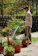 A happy gardener watering vibrant flower beds with a sleek green garden hose.
